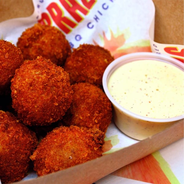 Crispy, golden-brown Peruvian croquettes with a side of creamy yellow dipping sauce in a Brazas BBQ Chicken container.