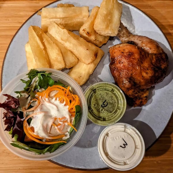 Peruvian BBQ chicken with yuca fries, a side salad, and two small containers of sauce.