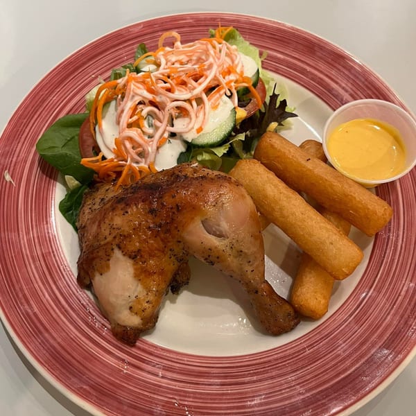 Peruvian roasted chicken leg and thigh, with a side of salad, fries, and yellow dipping sauce.