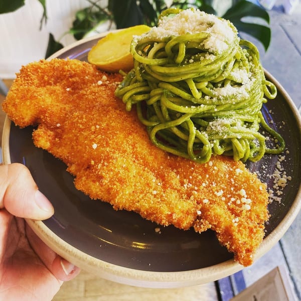 Crispy fried chicken milanese with green pesto spaghetti and a lemon wedge on a dark plate.