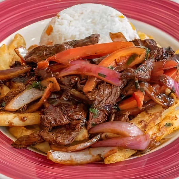 Peruvian Lomo Saltado with steak, red onions, tomatoes, french fries, and white rice on a red plate.