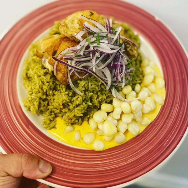 Peruvian Arroz con Pollo with fried chicken, red onion relish, and corn on a red-rimmed plate.