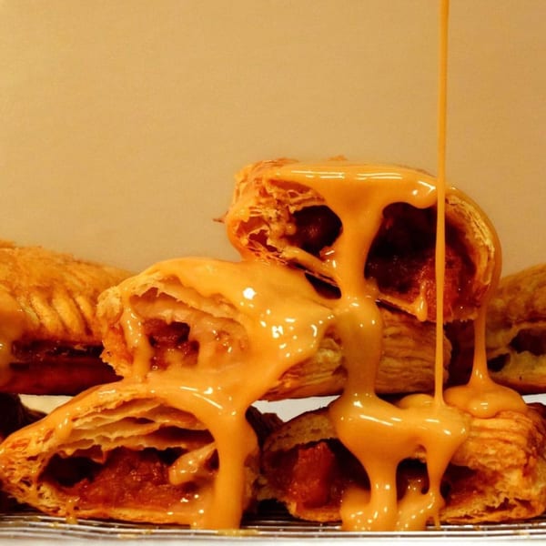 Peruvian empanadas with a rich, golden sauce drizzled over them, showcasing flaky pastry and savory filling.