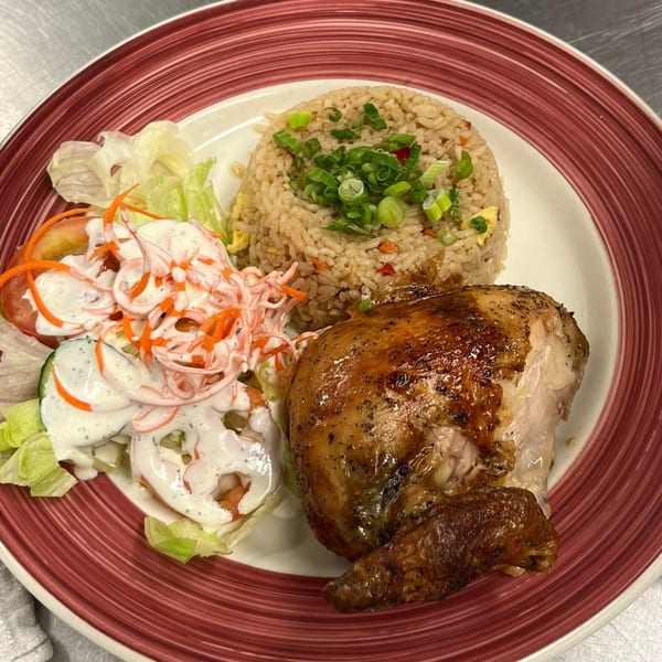 Peruvian rotisserie chicken with fried rice and a side salad on a red-rimmed plate.