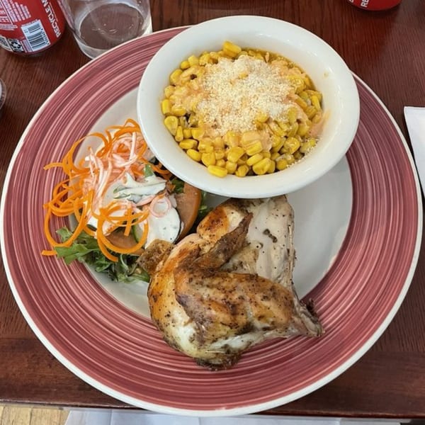 Peruvian BBQ chicken with a side of corn, salad, and shredded carrots on a red-rimmed plate.
